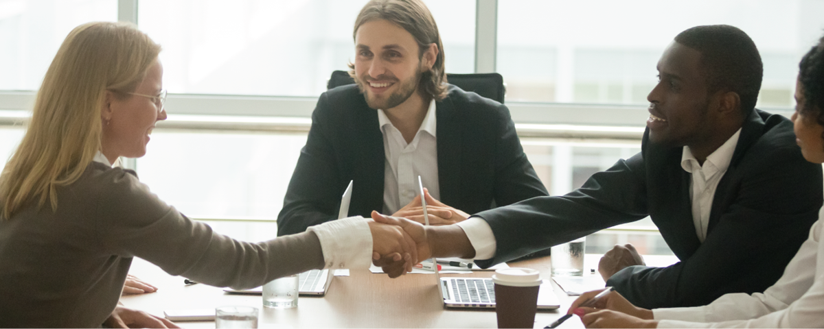 group of colleagues around a table while two shake hands