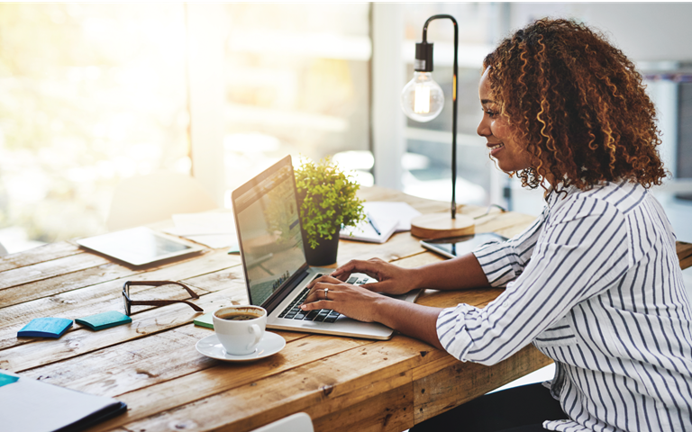 woman in striped shirt sitting at her desk on her laptop in bright office