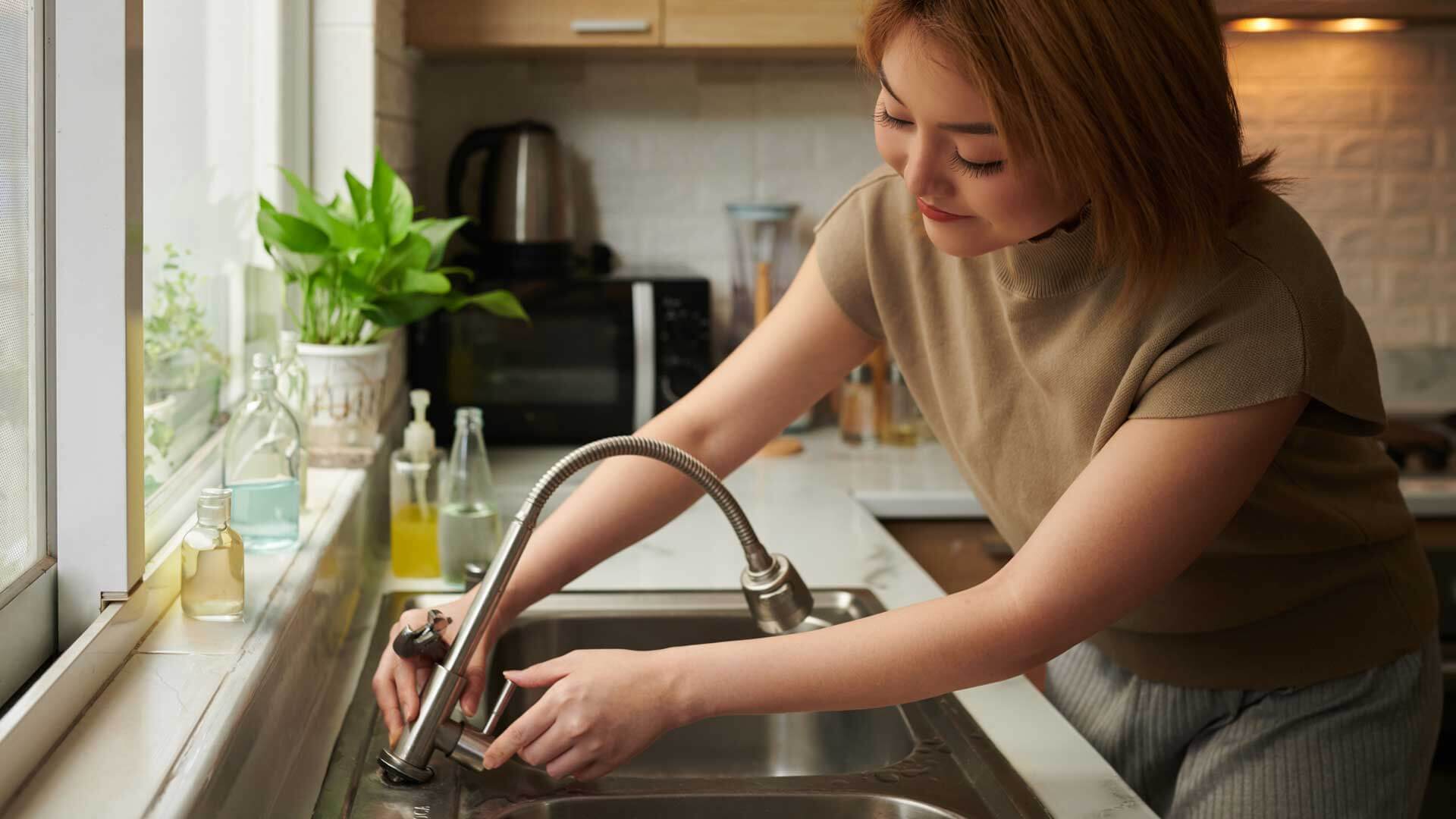 Female using sink faucet and exploring faucet technologies to combat the global water crises.