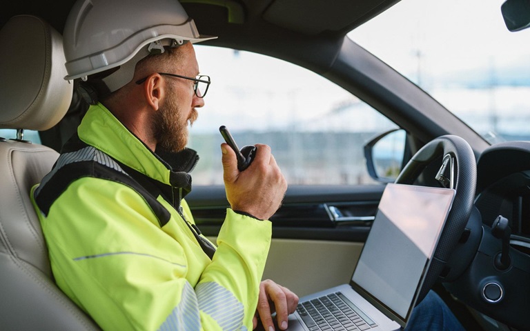 Young male electrical engineer working with walkie talkie and laptop in his car