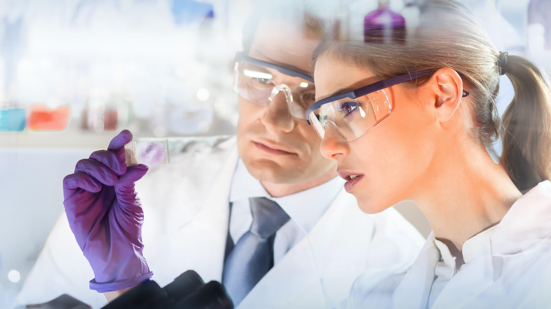 Male and female medical experts in safey goggles examining a test tube.