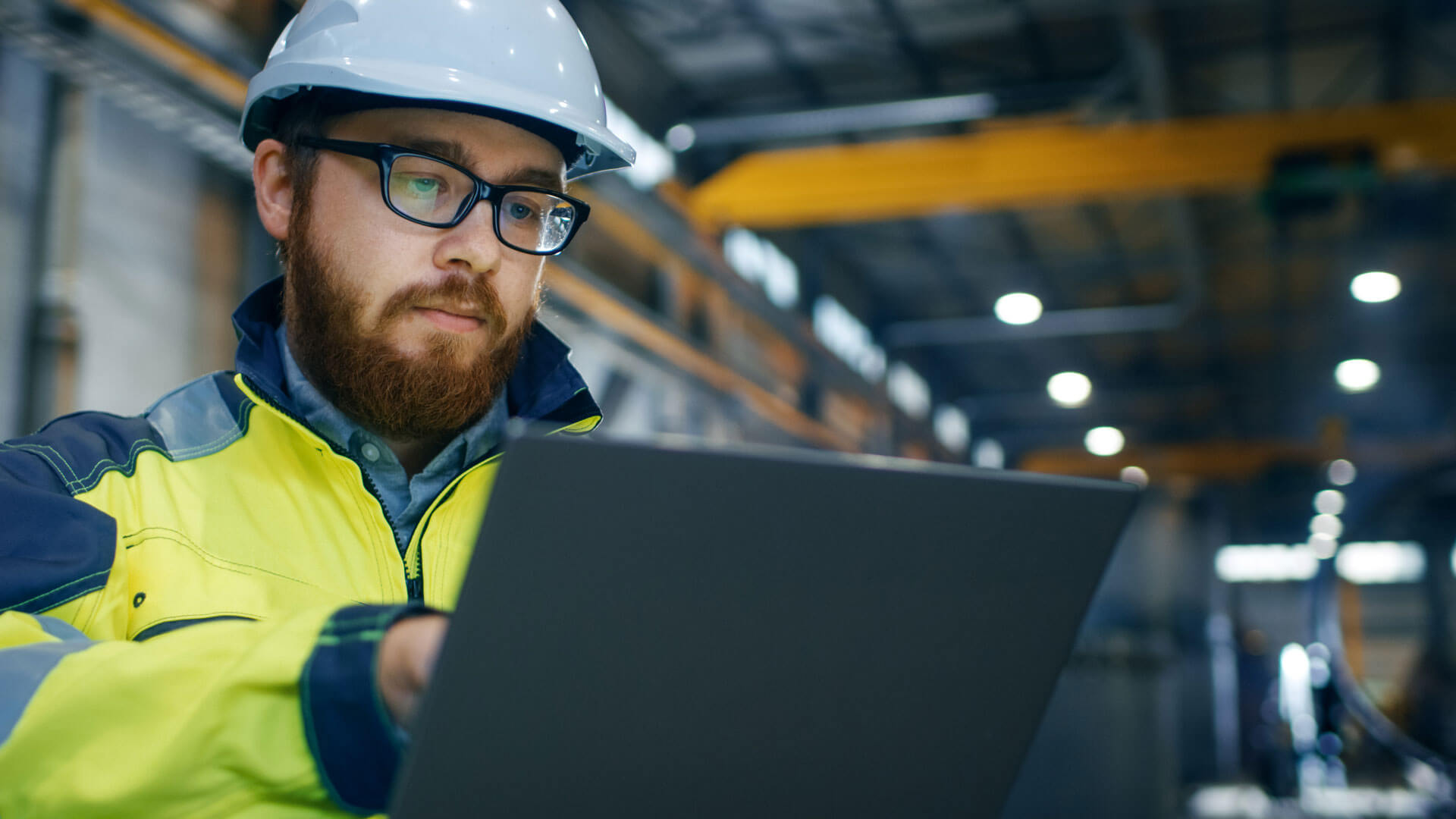 A male test engineer in a white hard hat gathering, analyzing, and compiling test data.