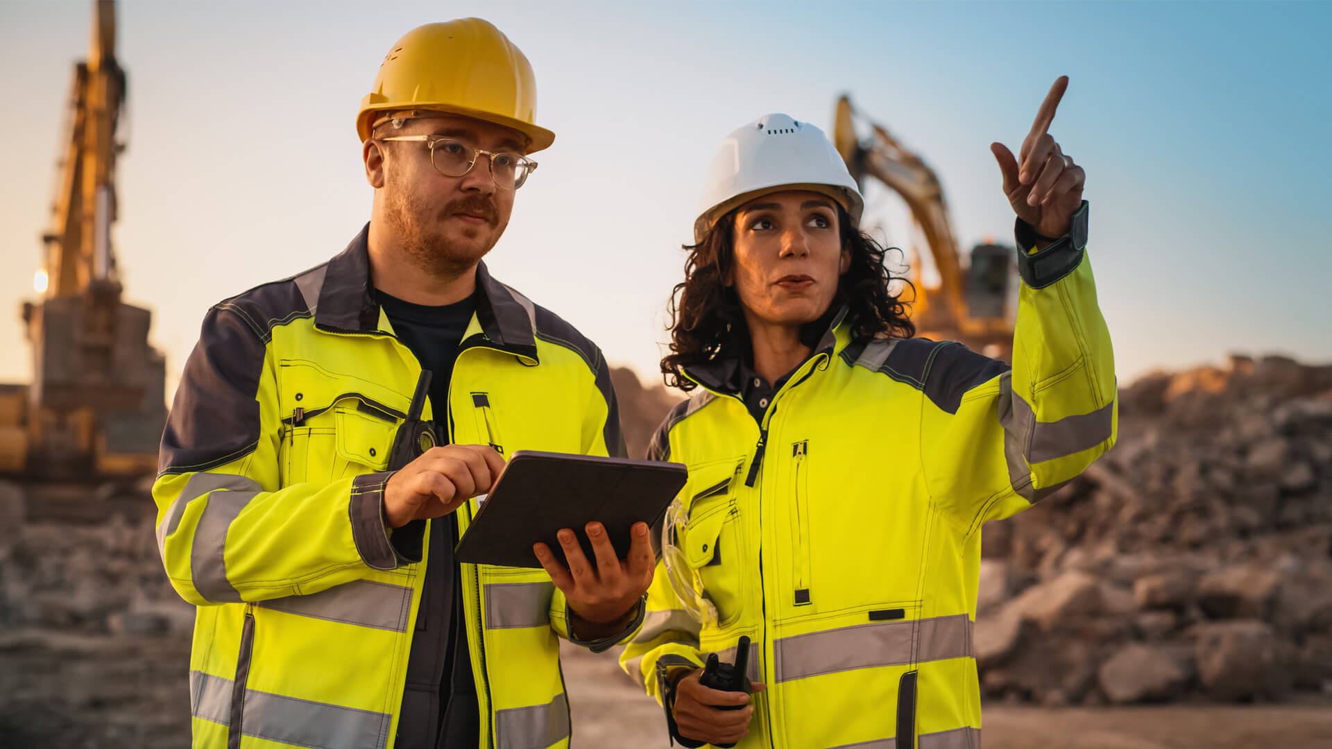 Construction worker and project safety manager reviewing a manufacturing project expansion plan on the construction site.