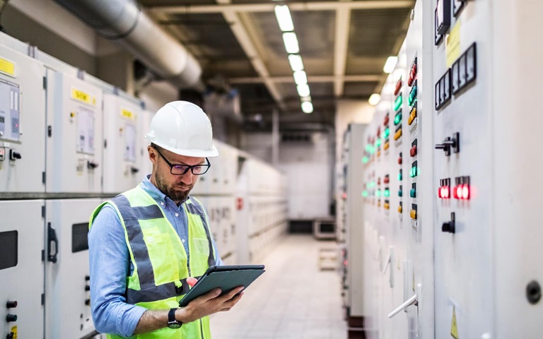 man wearing protective gear holding tablet in utility engineering control room