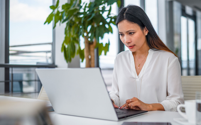 Female executive sitting at the desk in a big bright spacious office using a laptop for her work